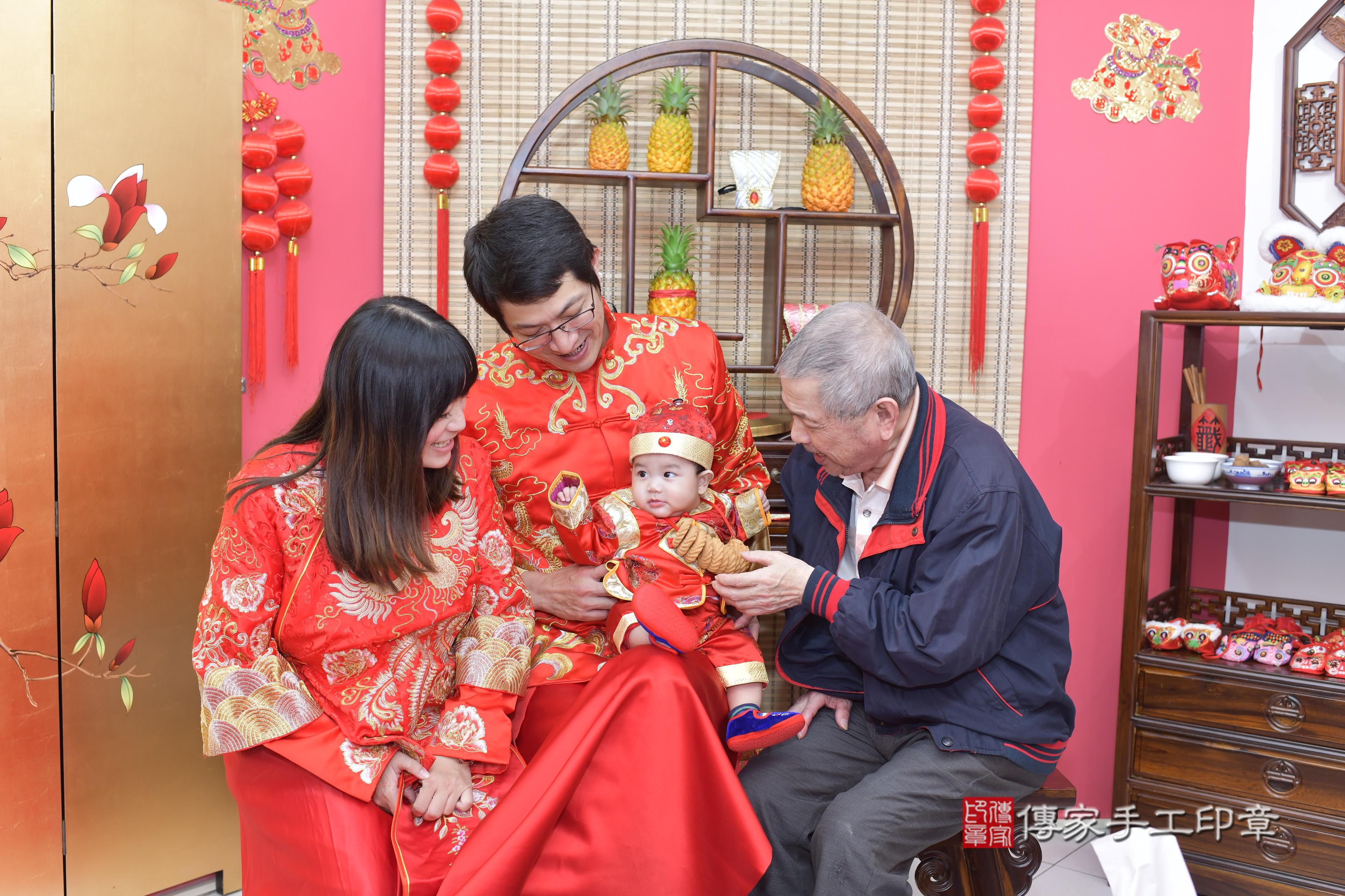 一家人一起穿著一套刺繡精美的紅色唐裝，笑容甜美，萌態十足。 這樣的傳統服飾，不僅為儀式增添了文化色彩，也讓這一天的紀念照片更加生動。